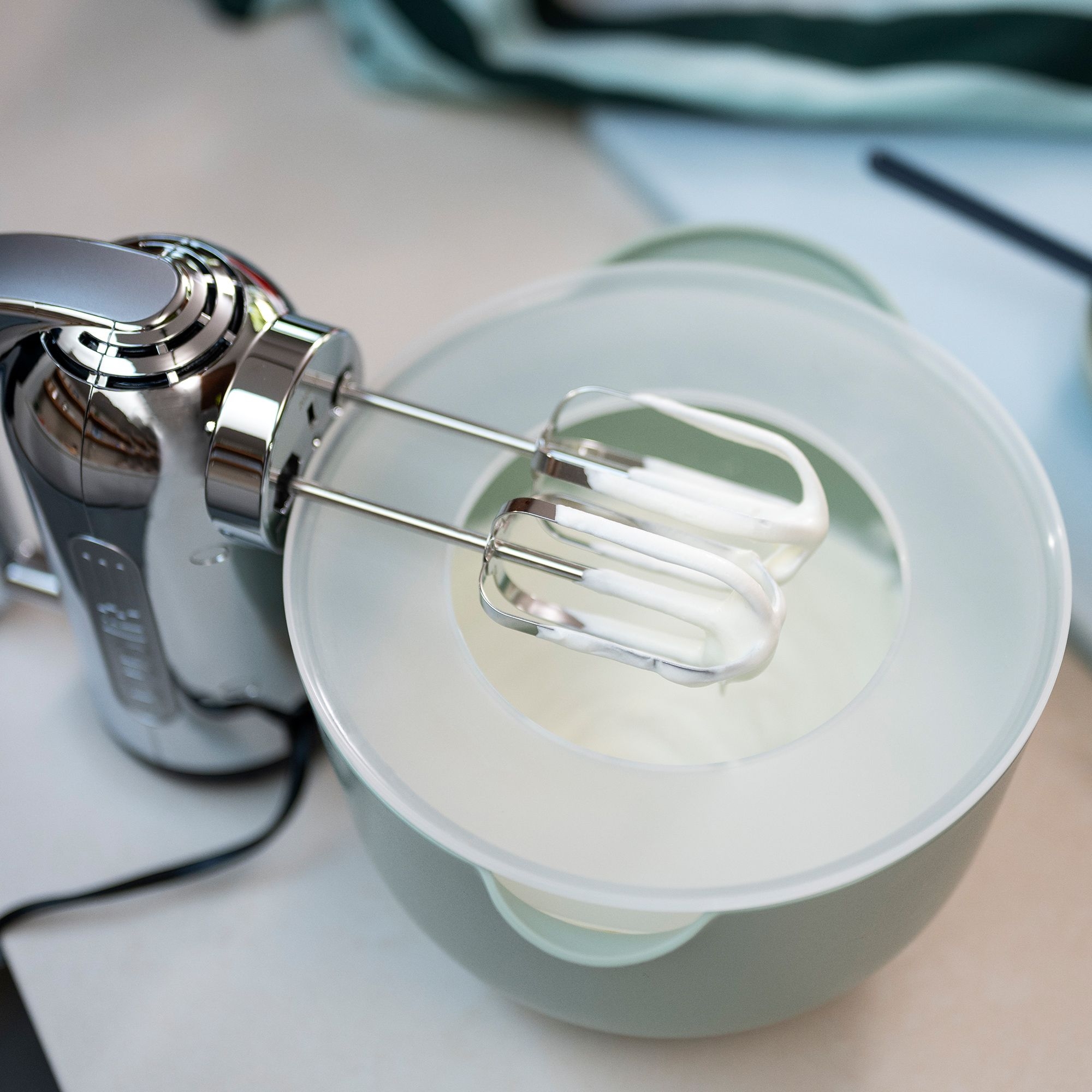 Silberner Handmixer schlägt Sahne in Schüssel