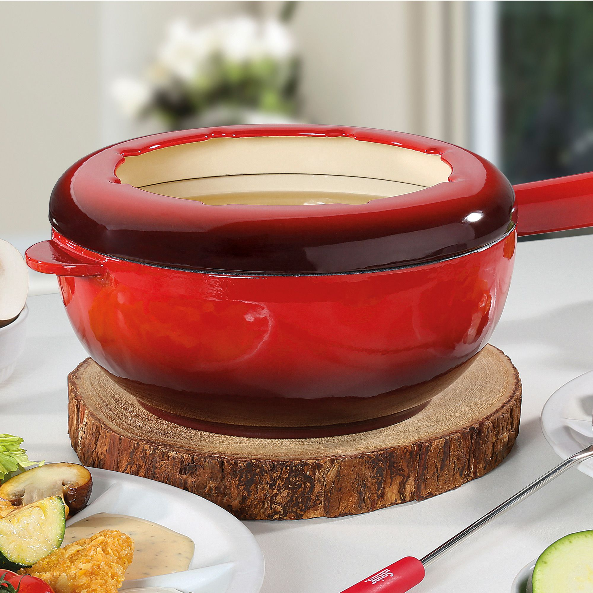 Red cast iron fondue pot on wooden trivet