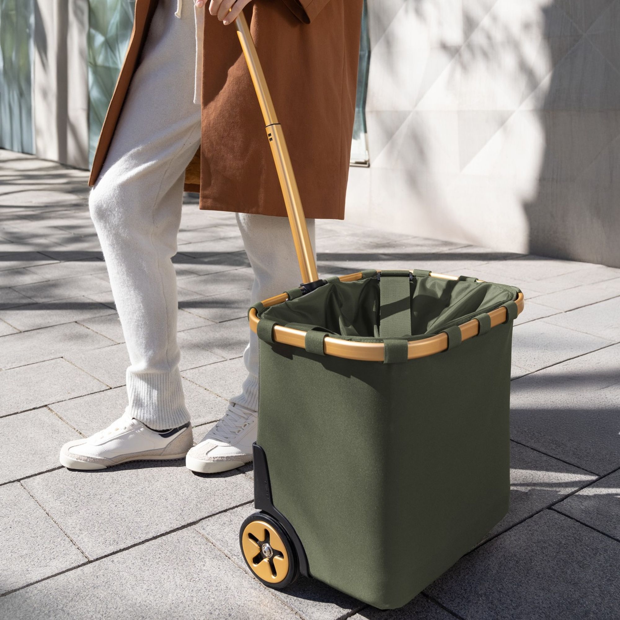 Person pulling foldable green shopping trolley in city