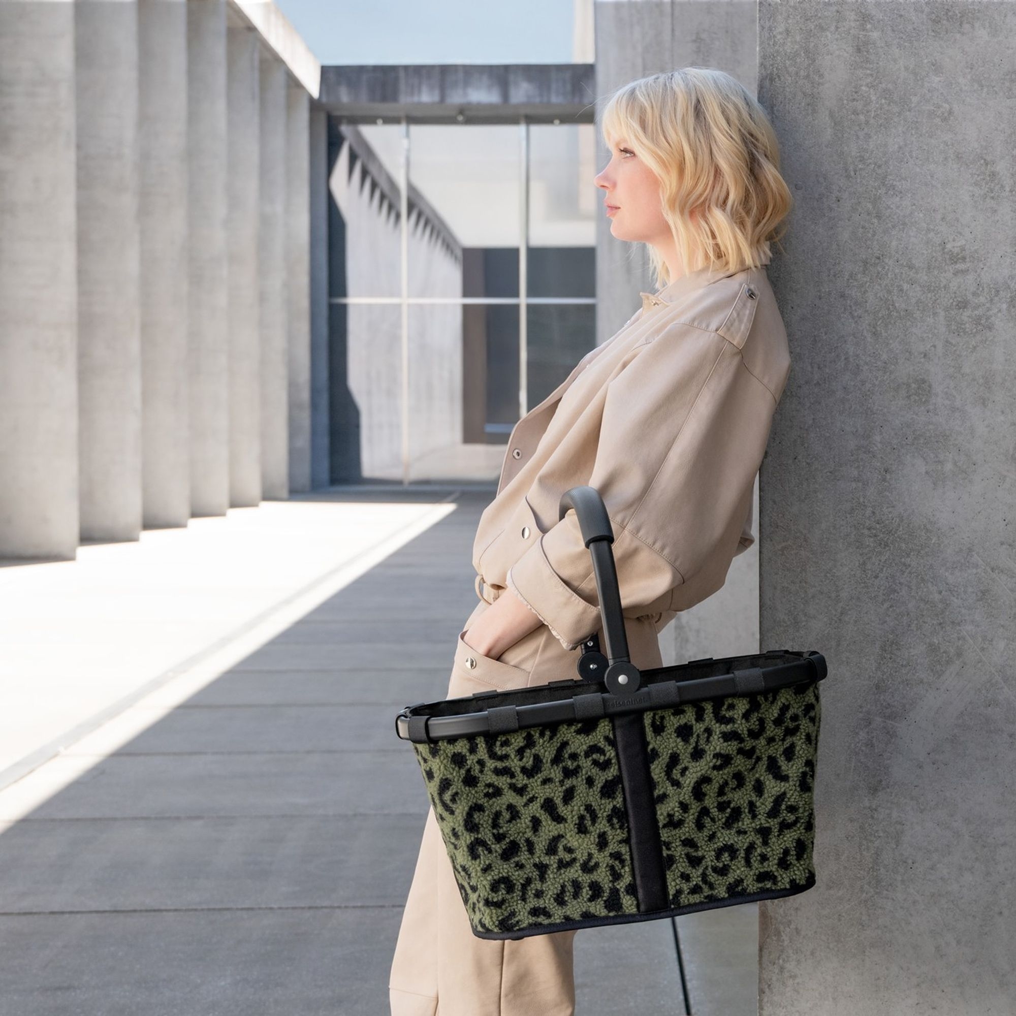 Frau lehnt an Wand mit grünem Einkaufskorb im Leopardenmuste