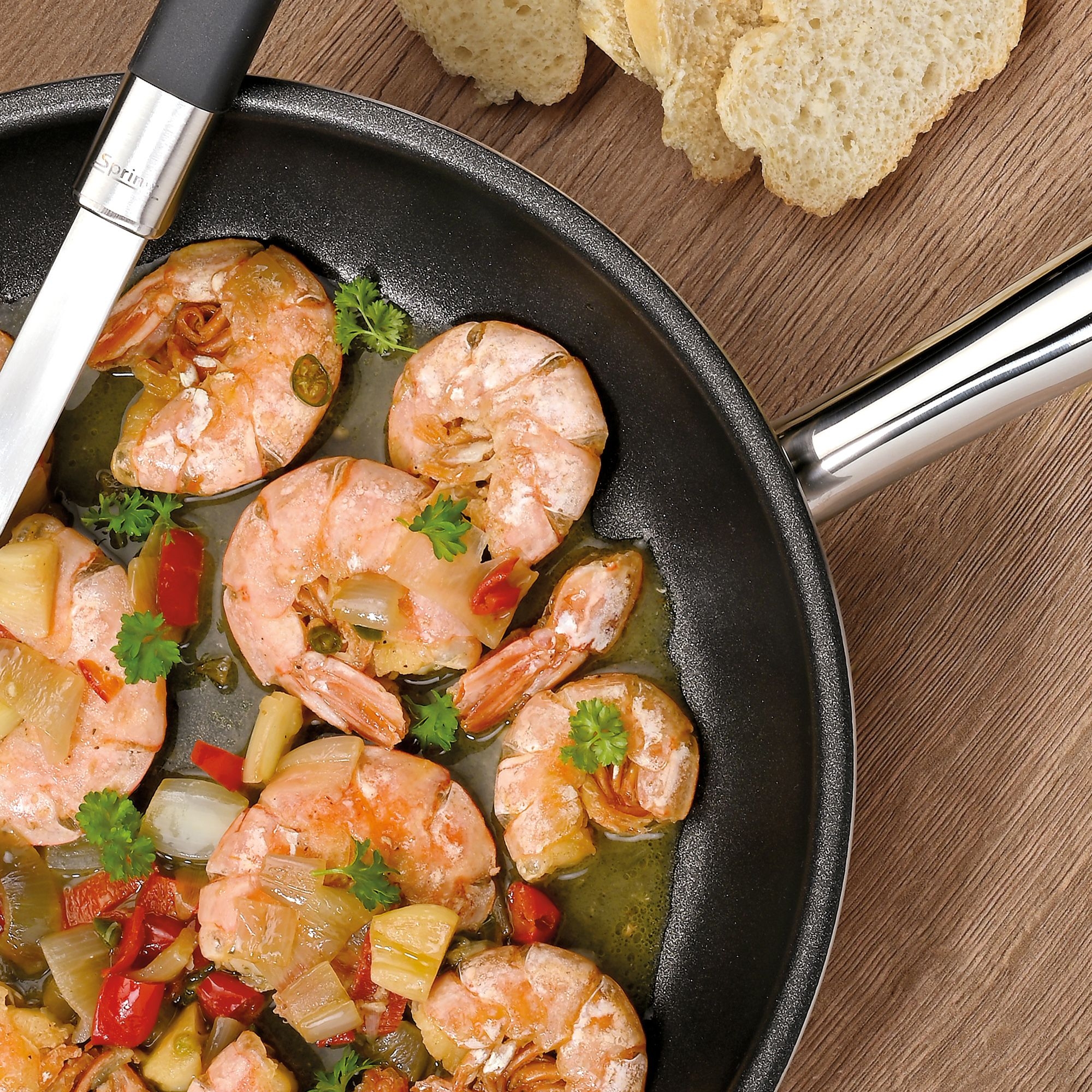 Prawns with vegetables in pan and bread on wooden table