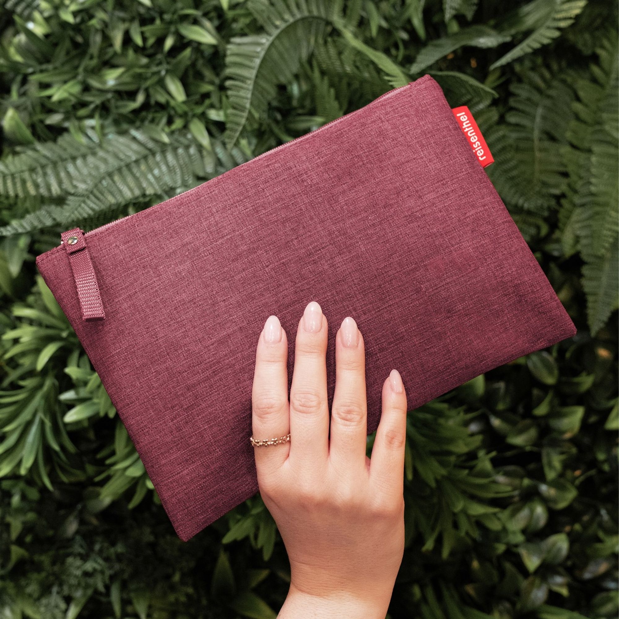 Hand holding burgundy pouch against greenery
