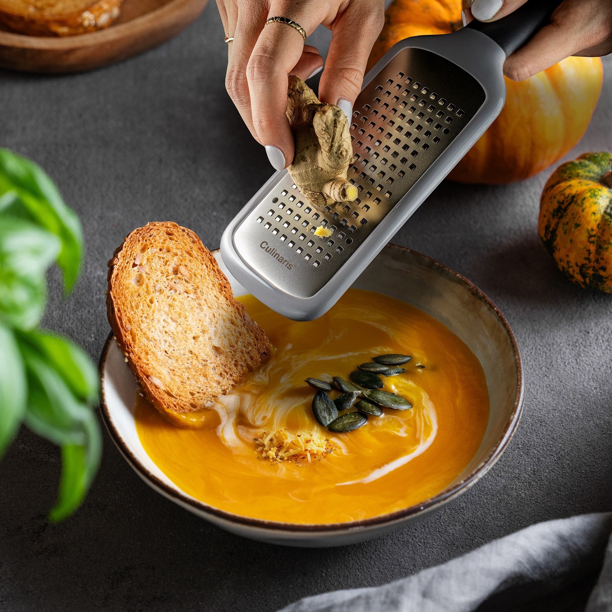 Hand reibt frischen Ingwer über cremige Kürbissuppe