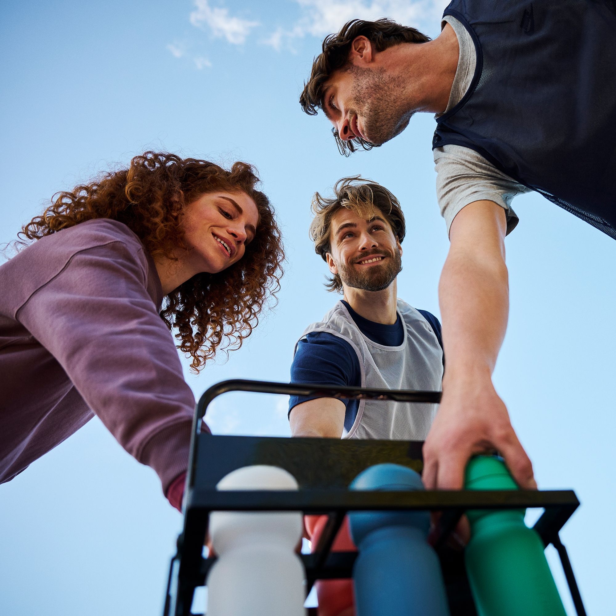 Drei Personen nehmen bunte Trinkflaschen aus Halterung