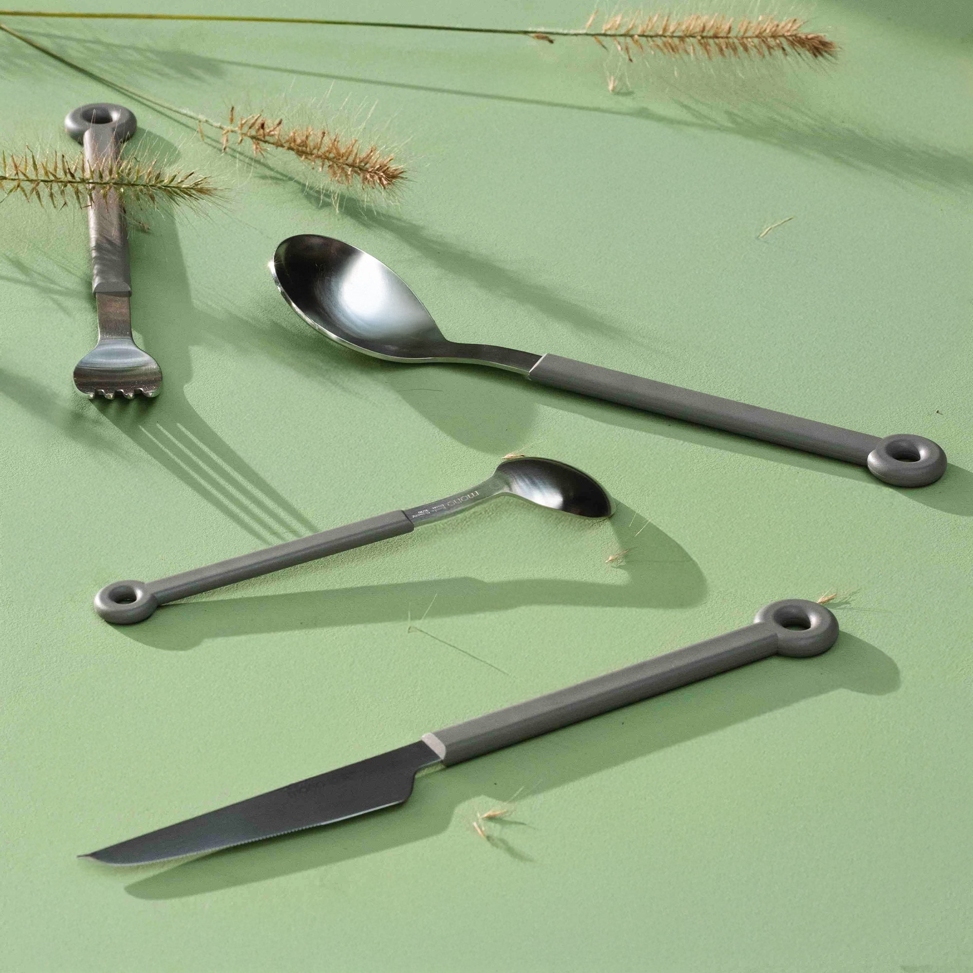 Vier graue Edelstahl-Besteckteile auf grünem Untergrund