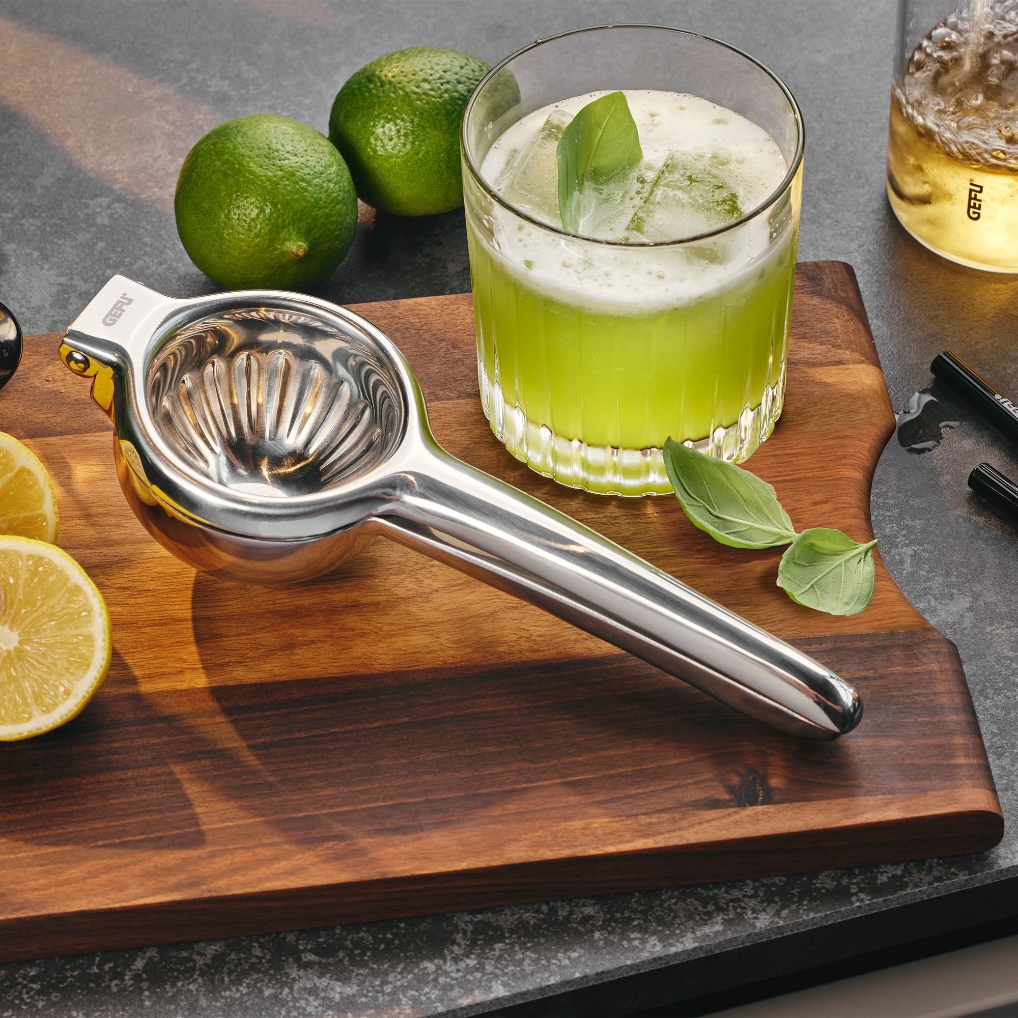 Stainless steel lemon squeezer on board with green cocktail