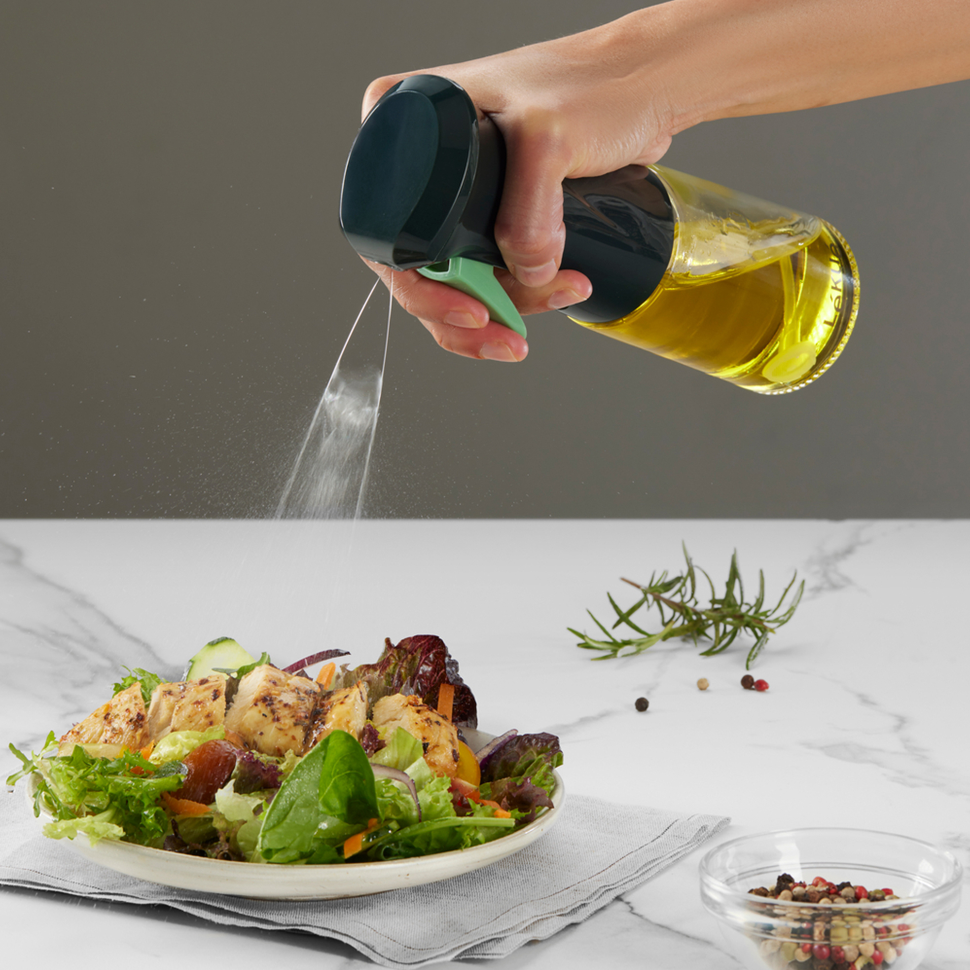 Hand spraying oil with dispenser onto fresh salad