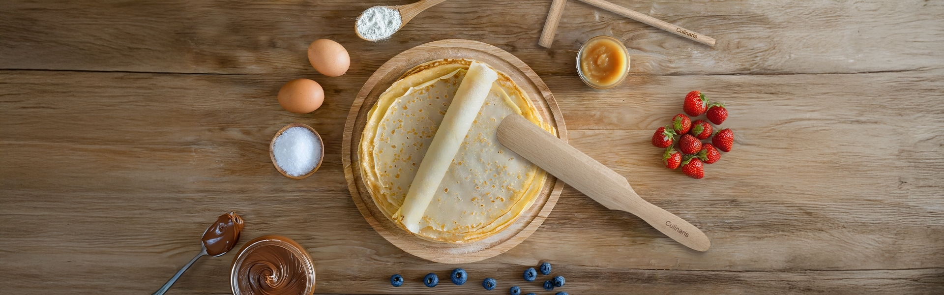 Crepes with wooden spatula, strawberries and ingredients
