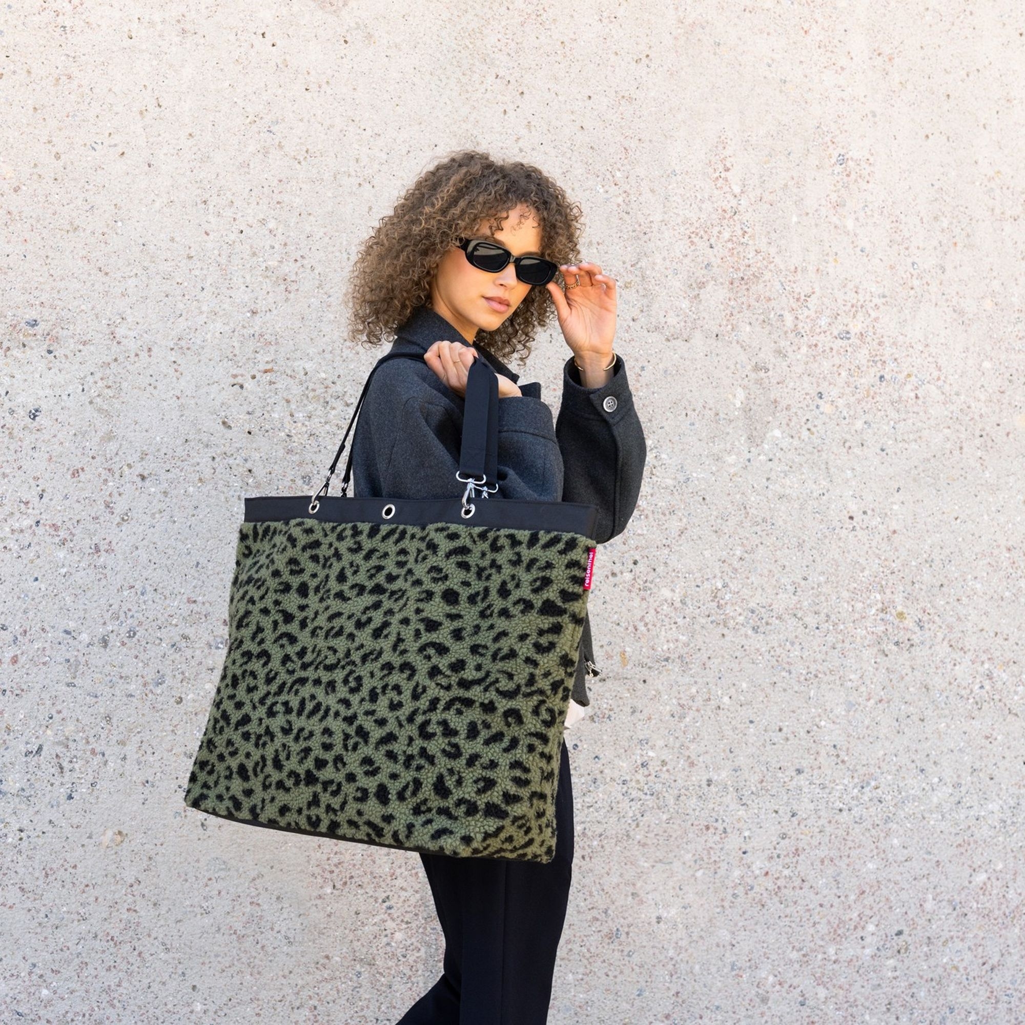 Woman with large green leopard print bag and sunglasses