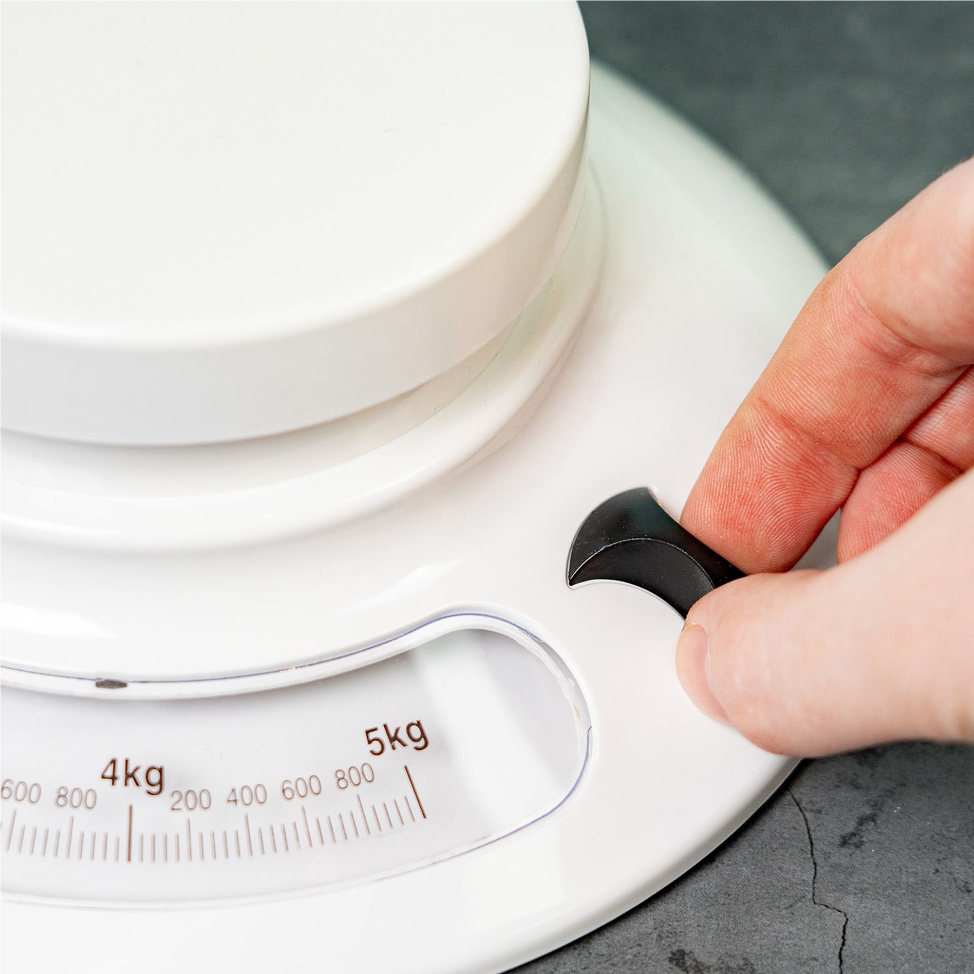 Hand adjusts mechanical tare on Westmark kitchen scale