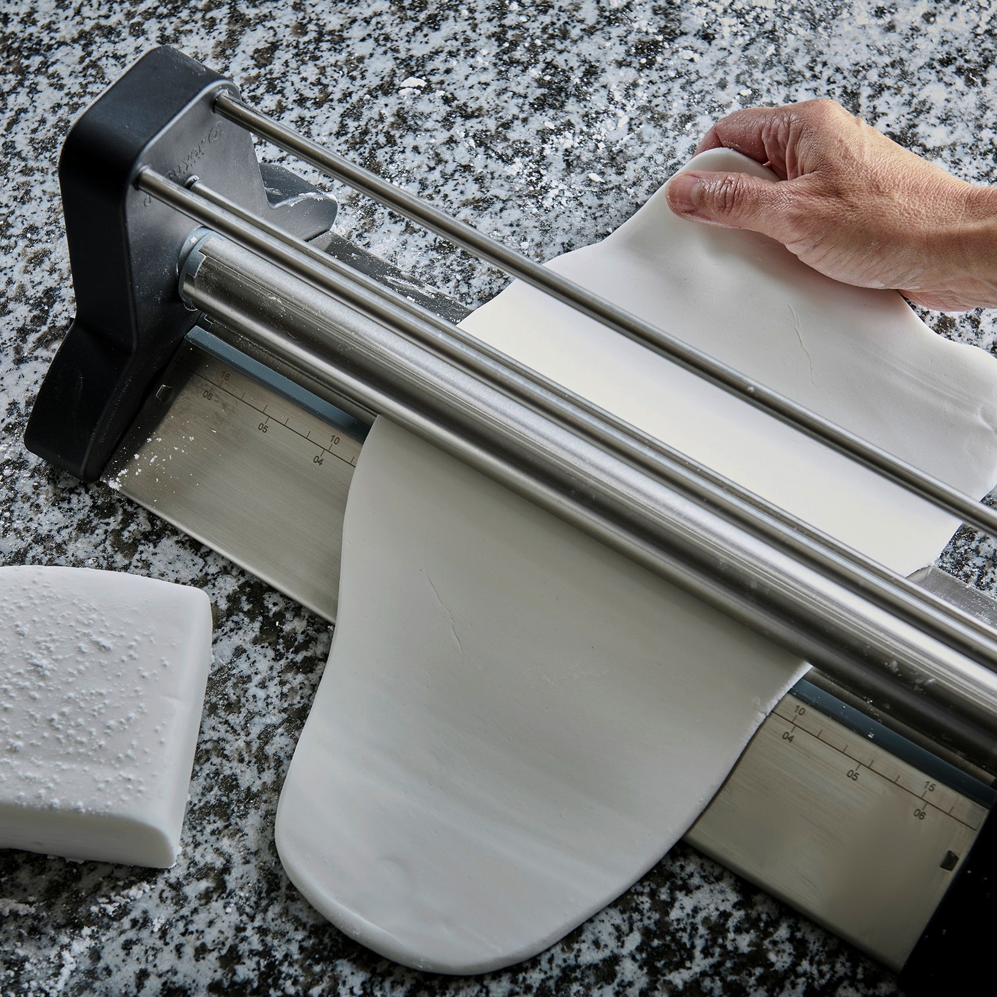 Hand guiding fondant through stainless steel cutter