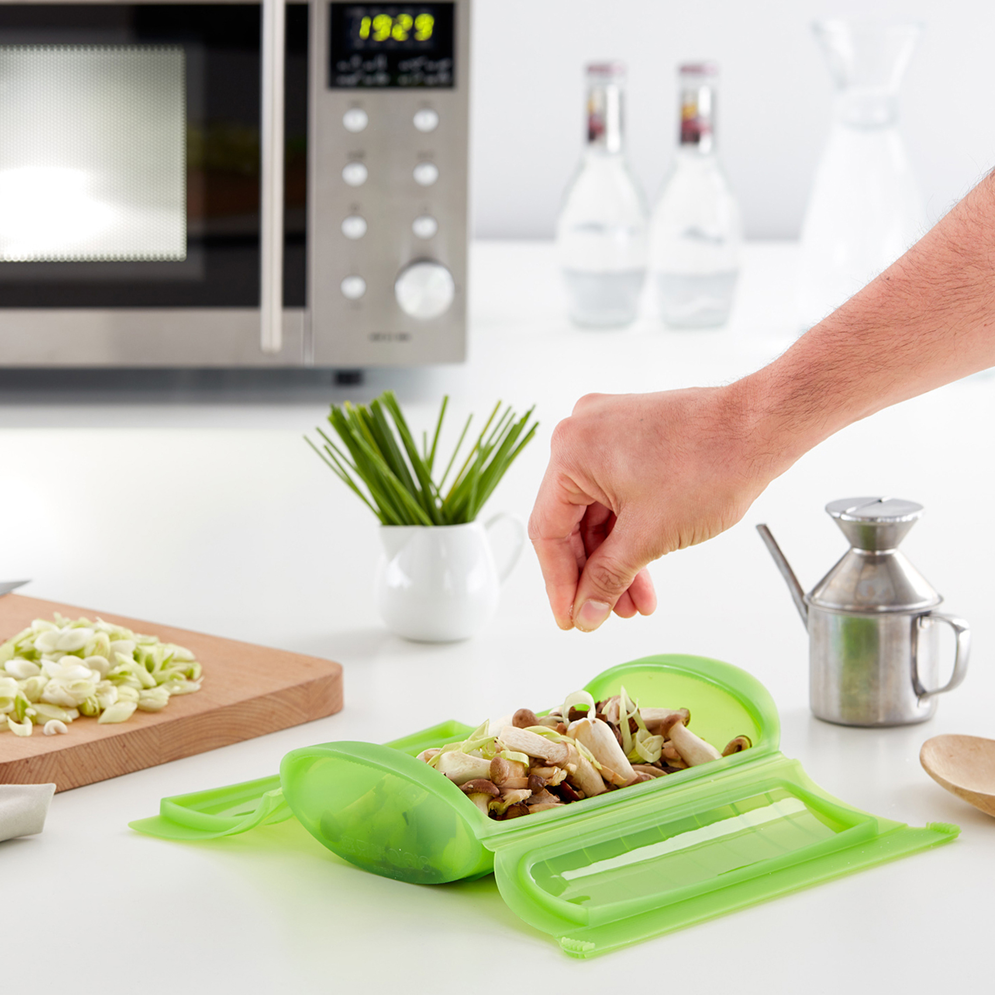 Hand filling green microwave steamer with vegetables