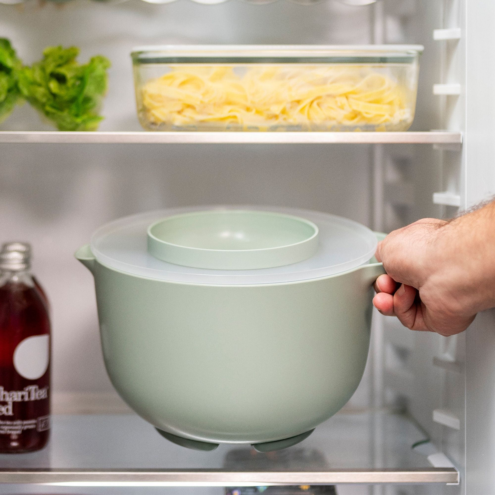 Hand stellt Vorratsschüssel mit Deckel in den Kühlschrank