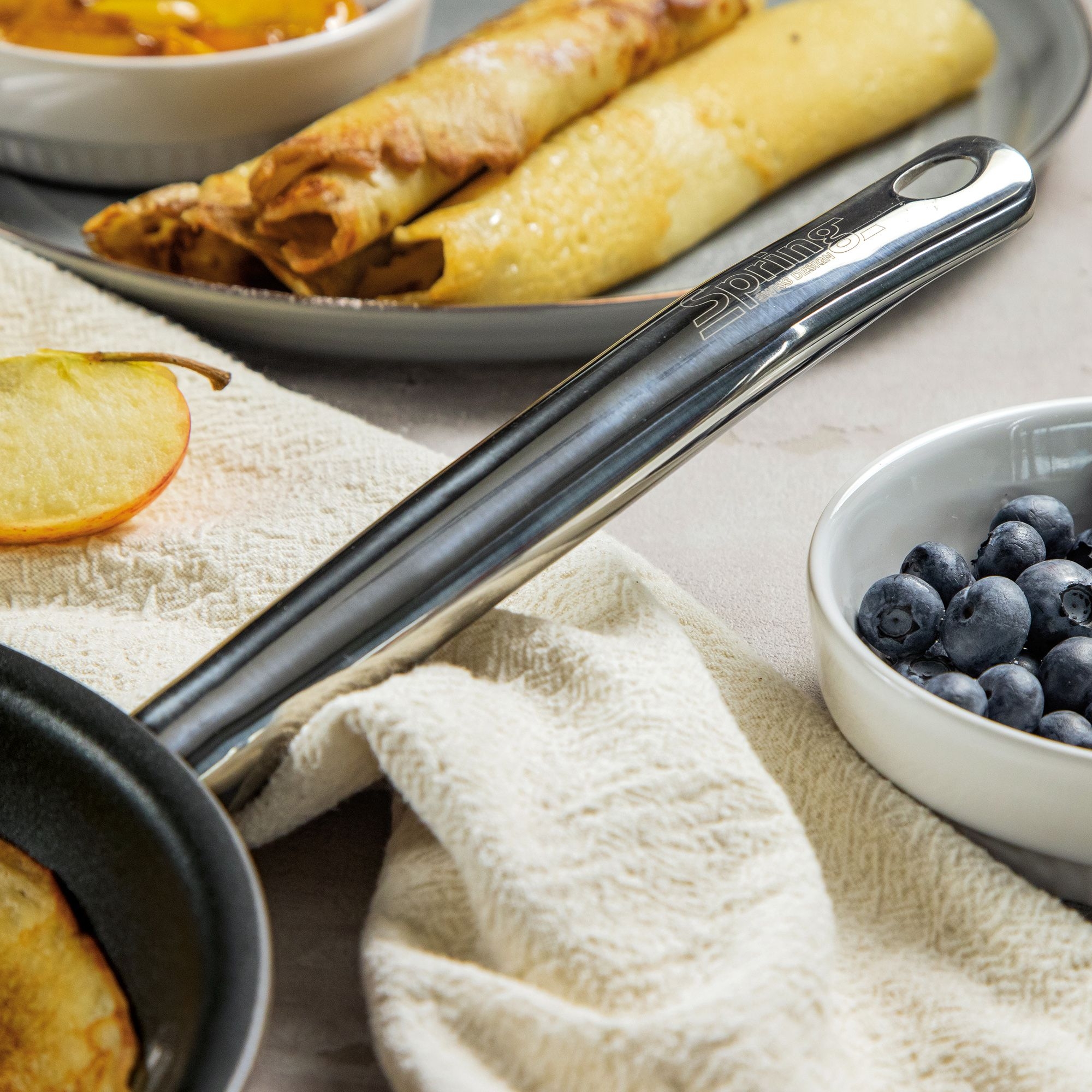 Stainless steel pan handle beside pancakes and berries
