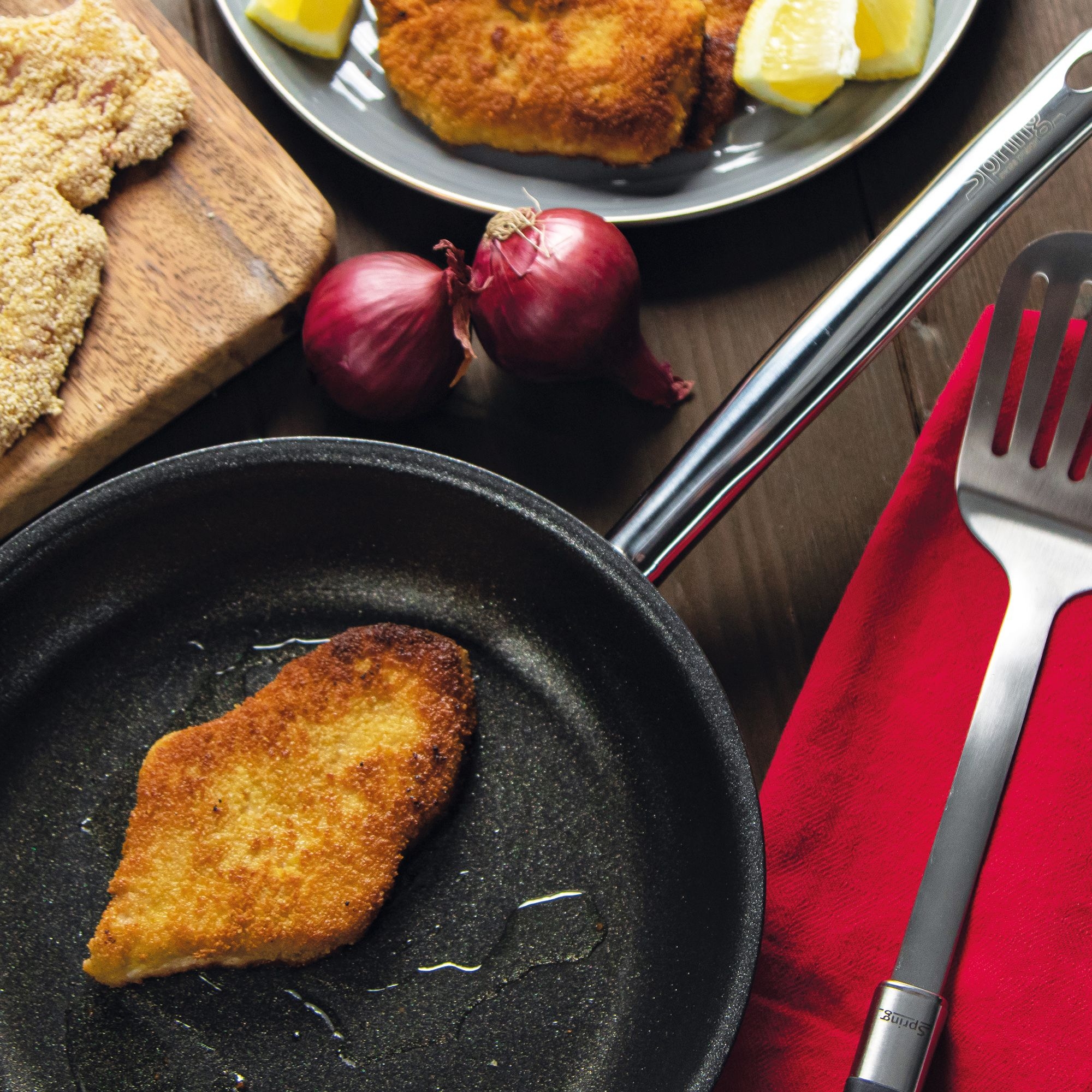 Golden brown schnitzel cooking in pan with fresh onions and