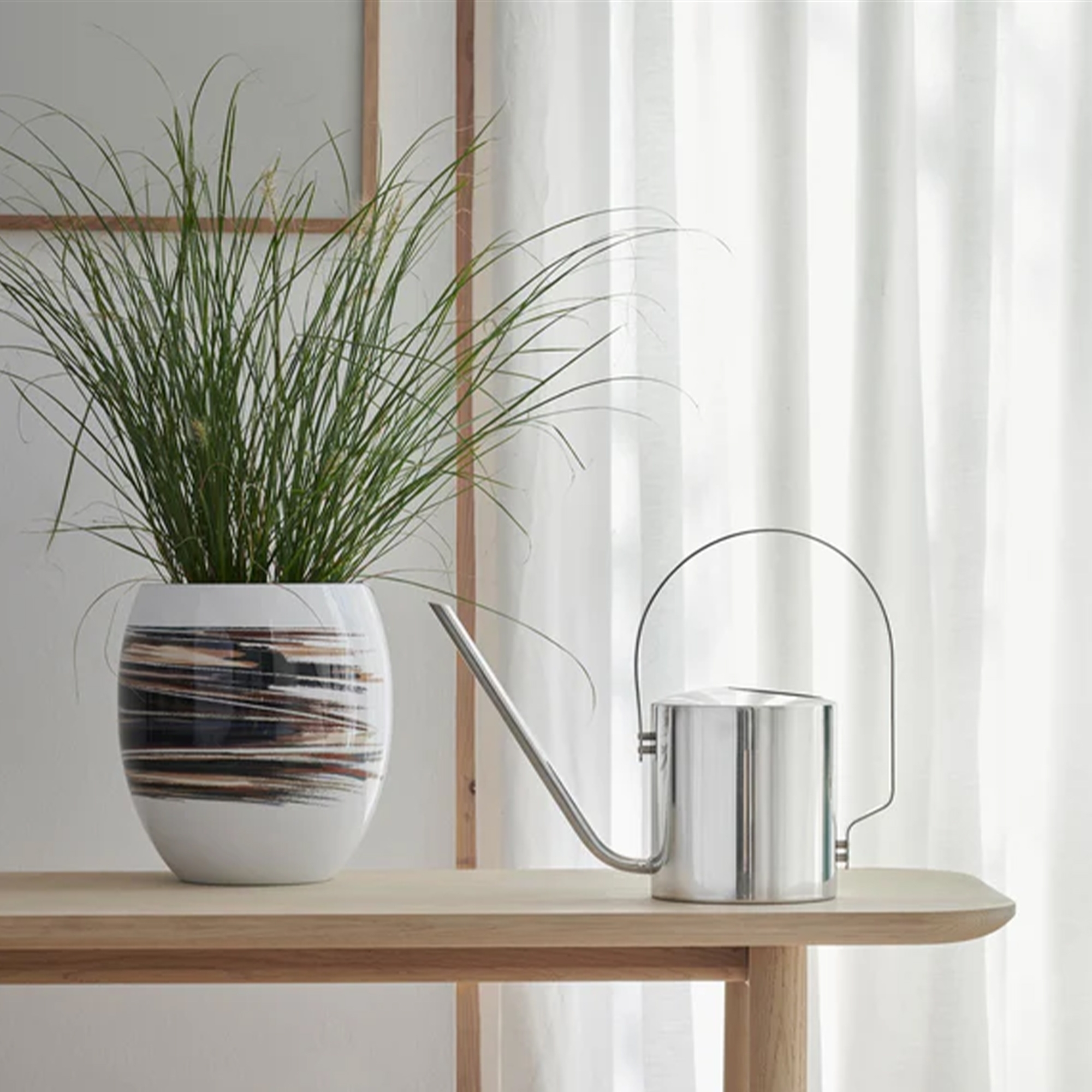 Silberne Edelstahl-Gießkanne neben Design-Blumentopf