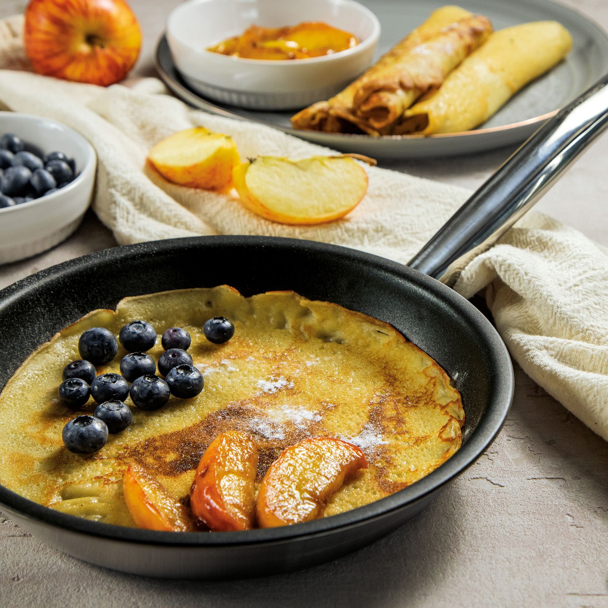 Pancake in pan with blueberries and caramelised apple slices