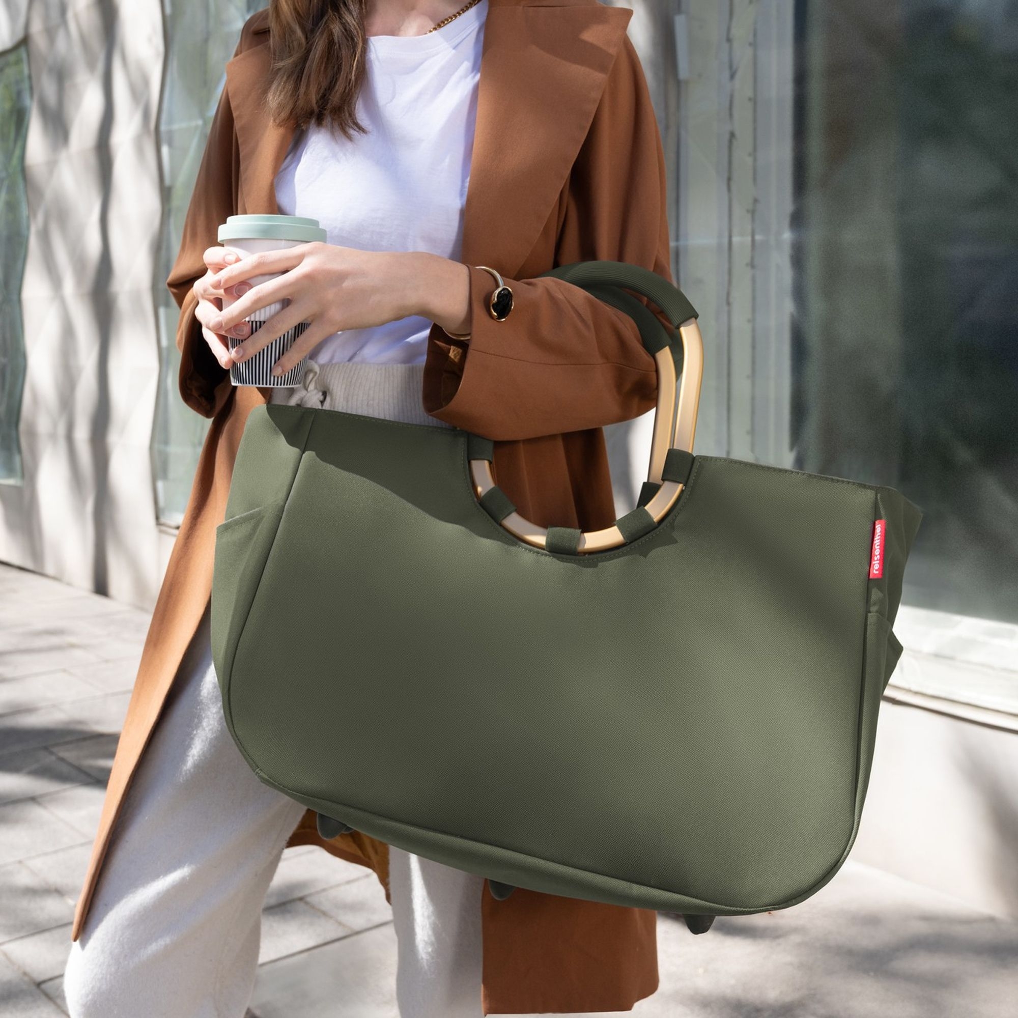 Woman with large olive green handbag and coffee cup
