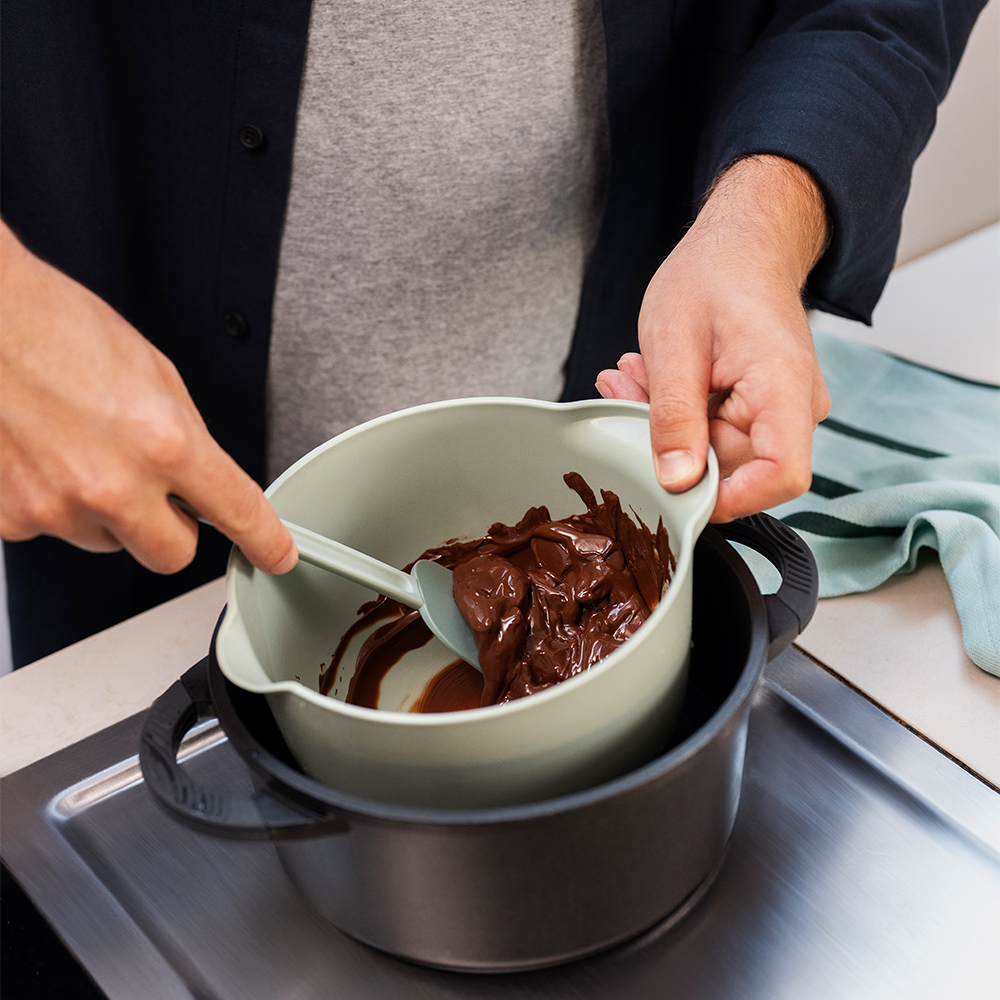 Person stirs chocolate in melting bowl over pot