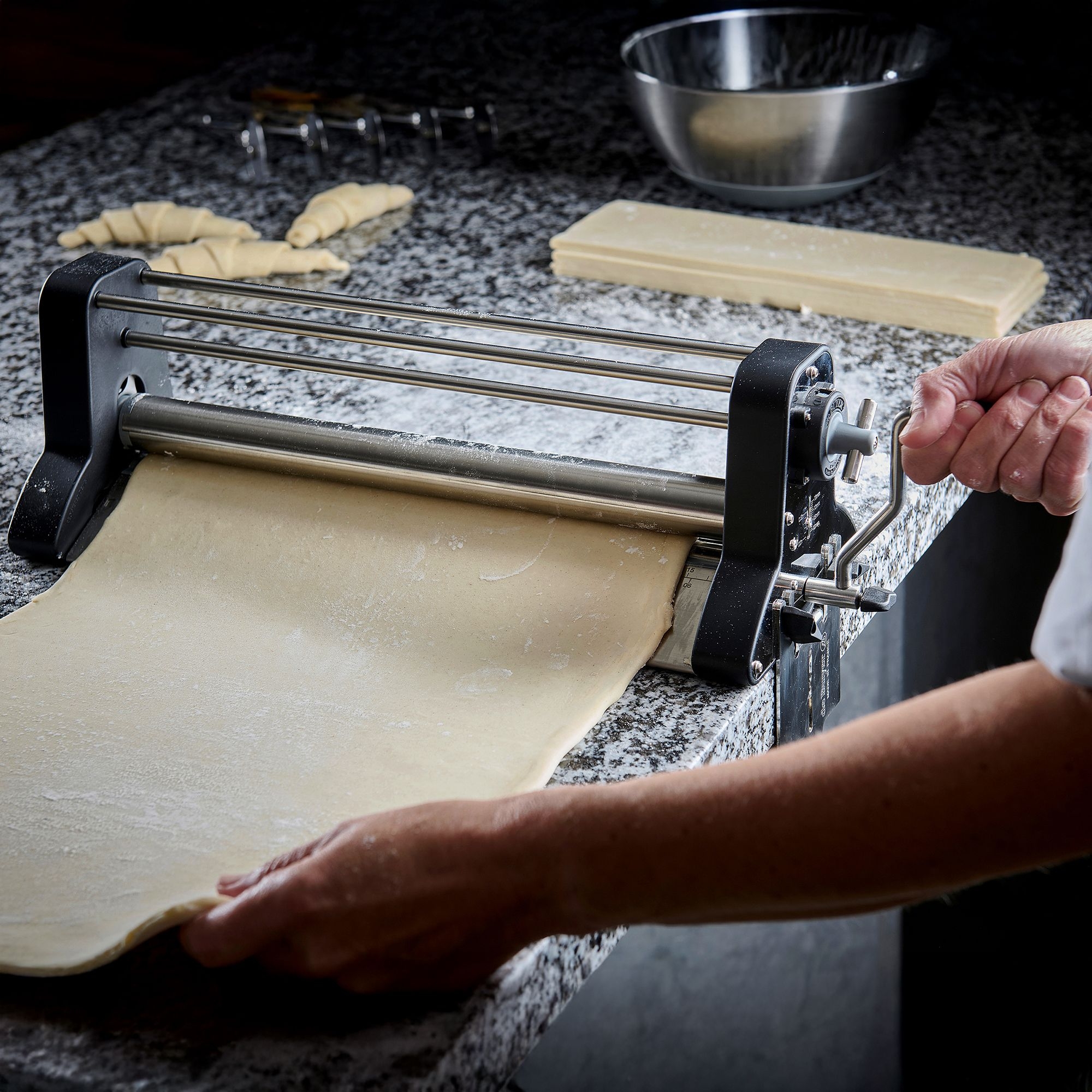 Baker rolling fresh dough with manual dough sheeter
