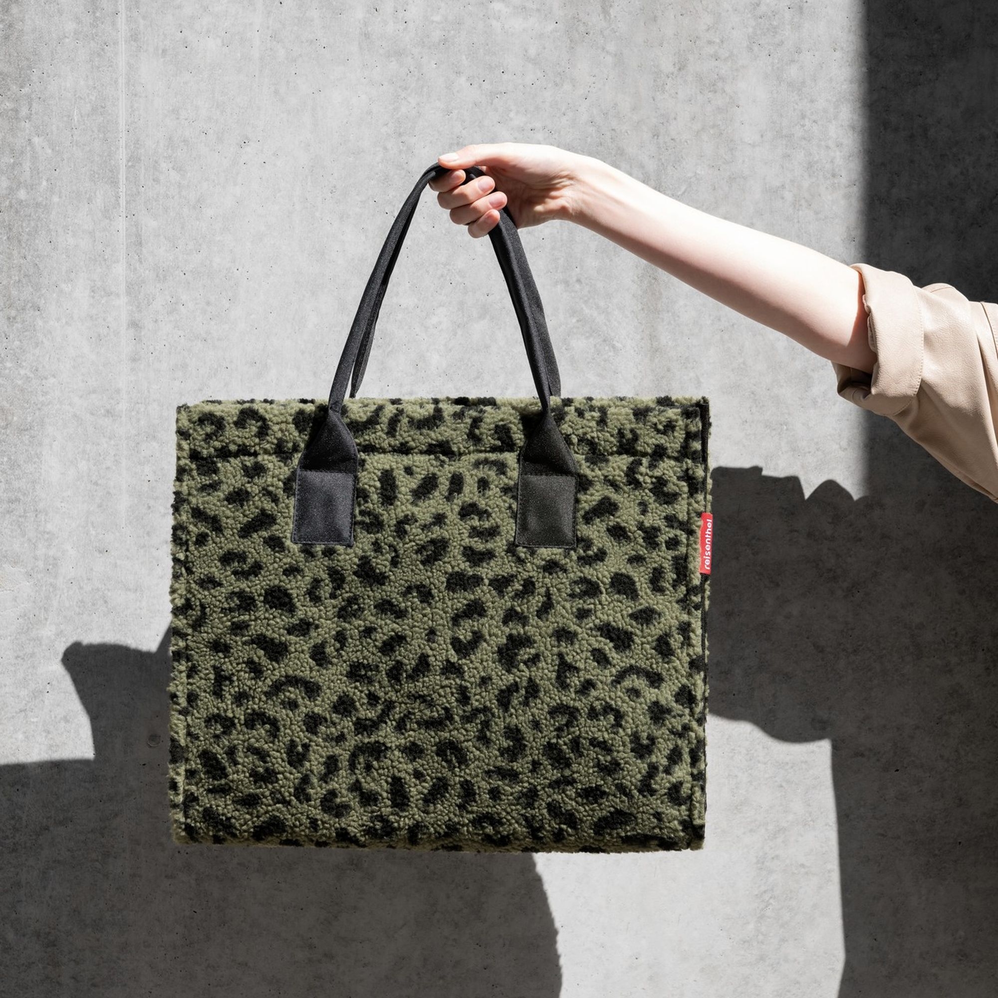 Hand holding green shopper bag with leopard print