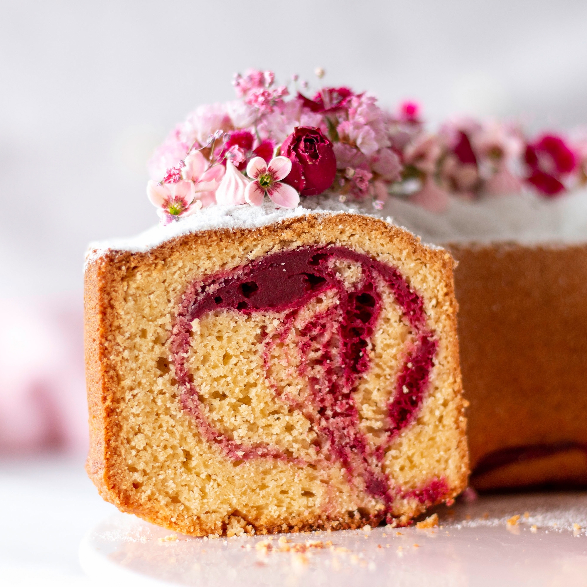 Aufgeschnittener Rührkuchen mit Himbeerswirl und Blüten