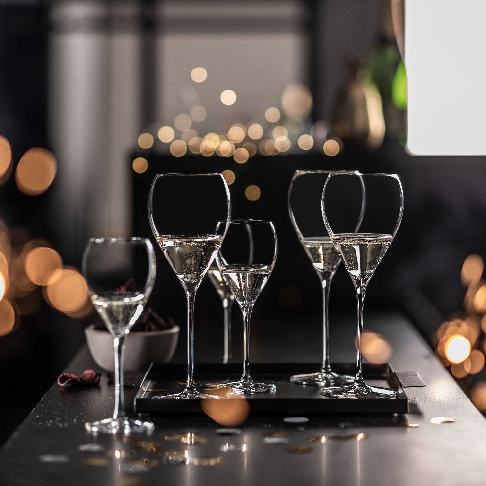 Five filled champagne flutes on tray in party setting