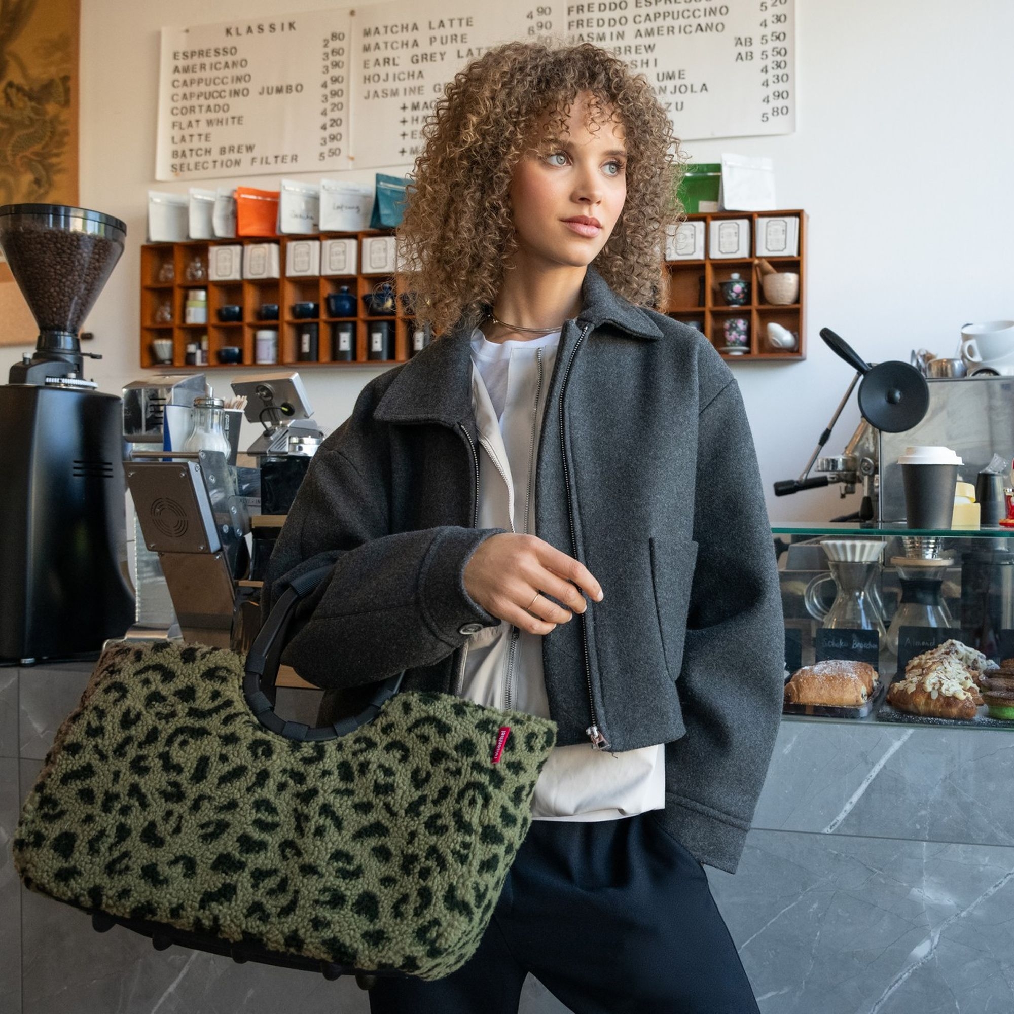 Woman with grey jacket and green leopard bag in café